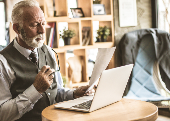 An experienced old businessman examining an agreement and working on his laptop.